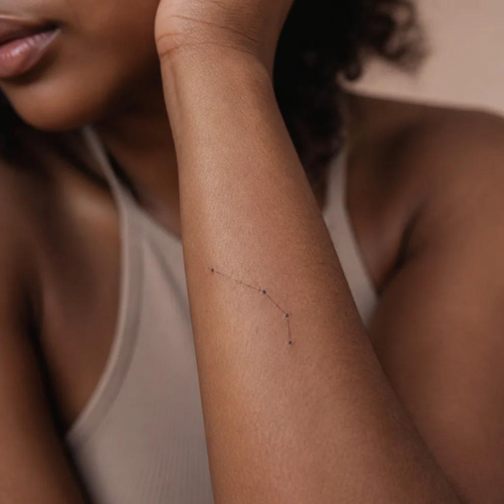 Delicate Aries constellation tattoo with small star dots and hairline connecting lines running along a woman's inner forearm