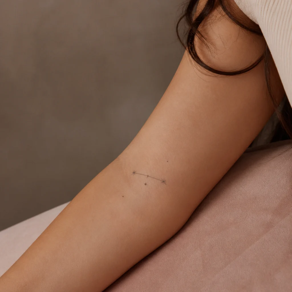 Delicate Aries constellation tattoo of connected stars in fine black lines running along a woman's forearm