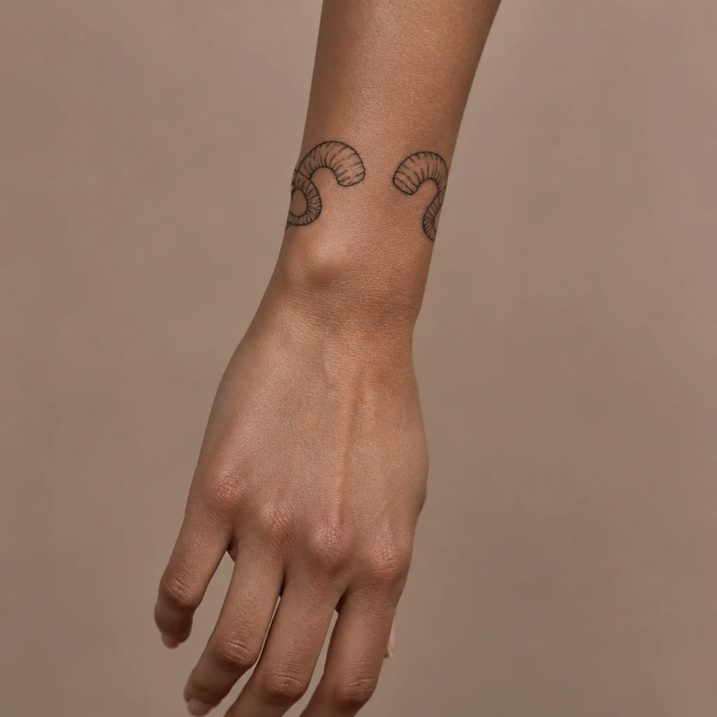 Aries ram horns tattoo curving gracefully around a woman's wrist like a fine-line bracelet