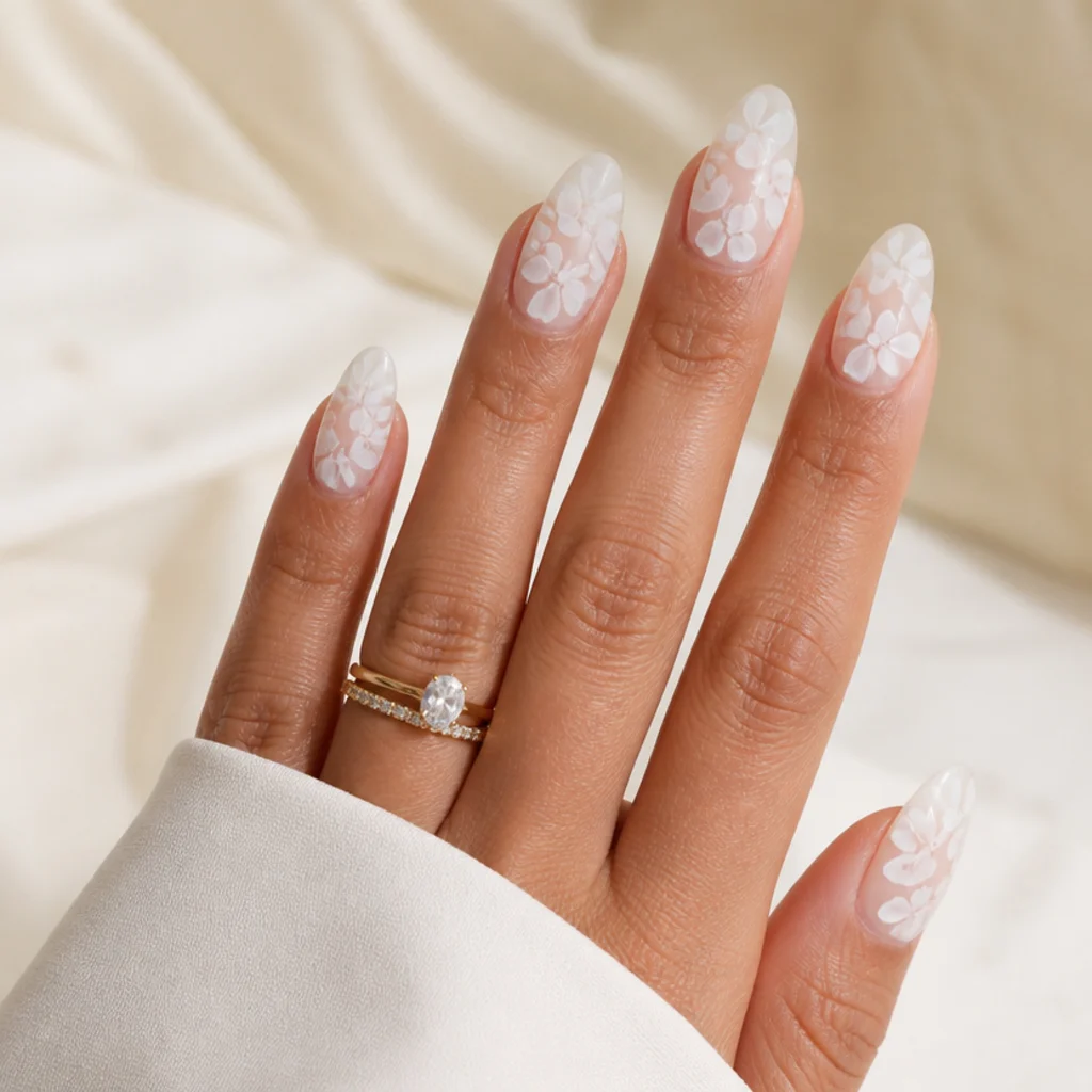 Long almond nails in an all-white bridal set with layered soft white blooming gel florals over a milky base